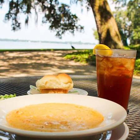 A bowl of seafood bisque on a metal table with Lake Peigneur in the background at Cafe Jefferson at Jefferson Island Rip Van Winkle Gardens