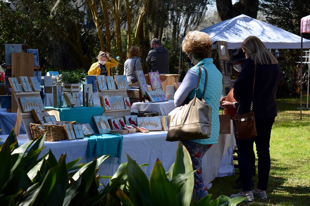 Masked people browse art on the lawn at the Shadows arts & Craft Fair